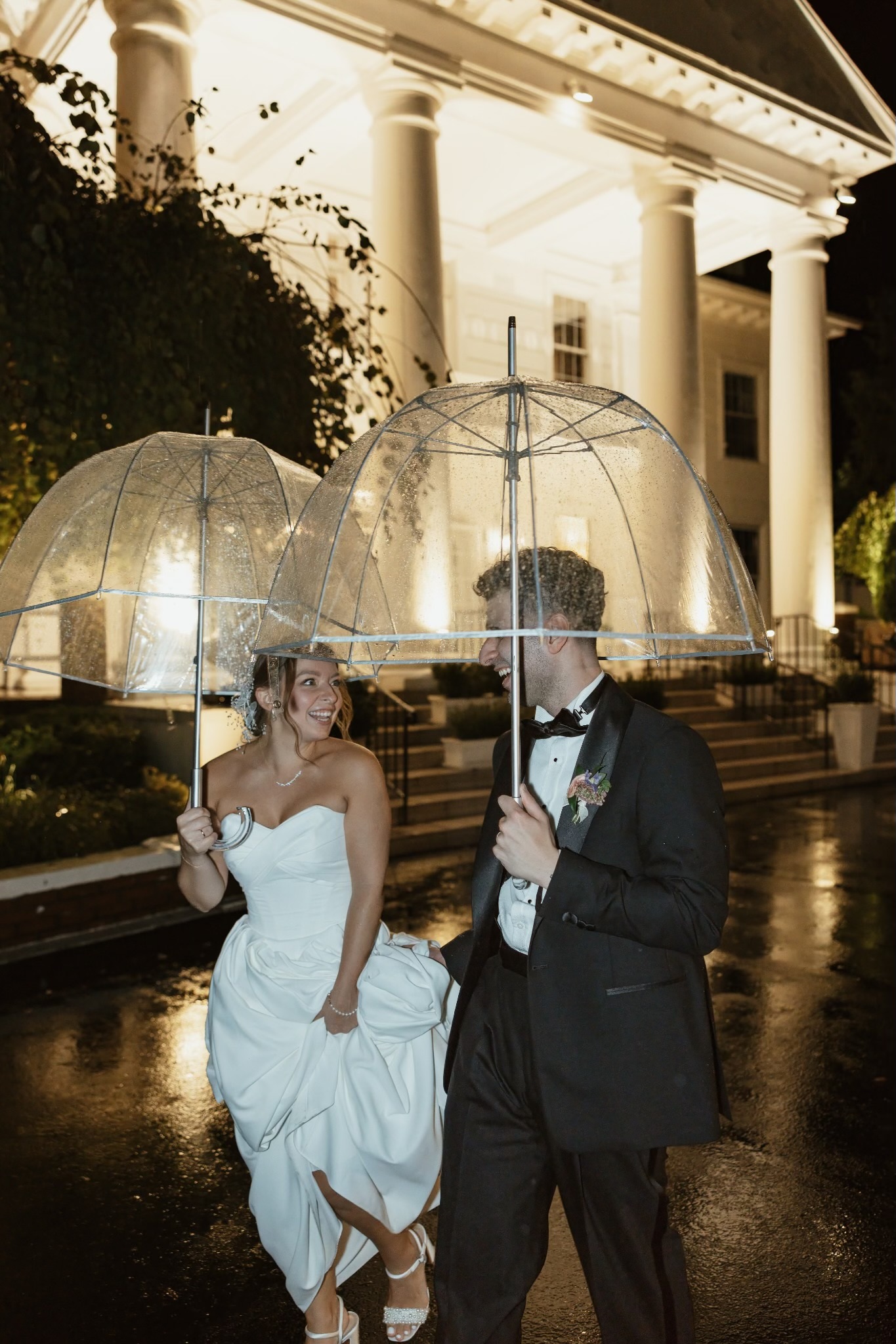 Giovanna and Milad beneath umbrellas outside the illuminated manor